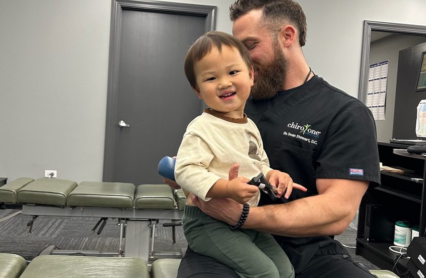 A smiling chiropractor holding a happy toddler during a clinic visit.