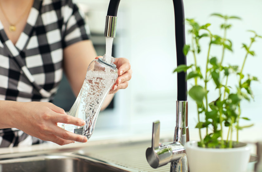 A person filling a water bottle at a sink to highlight the importance of hydration for maintaining a balanced pH level and overall health