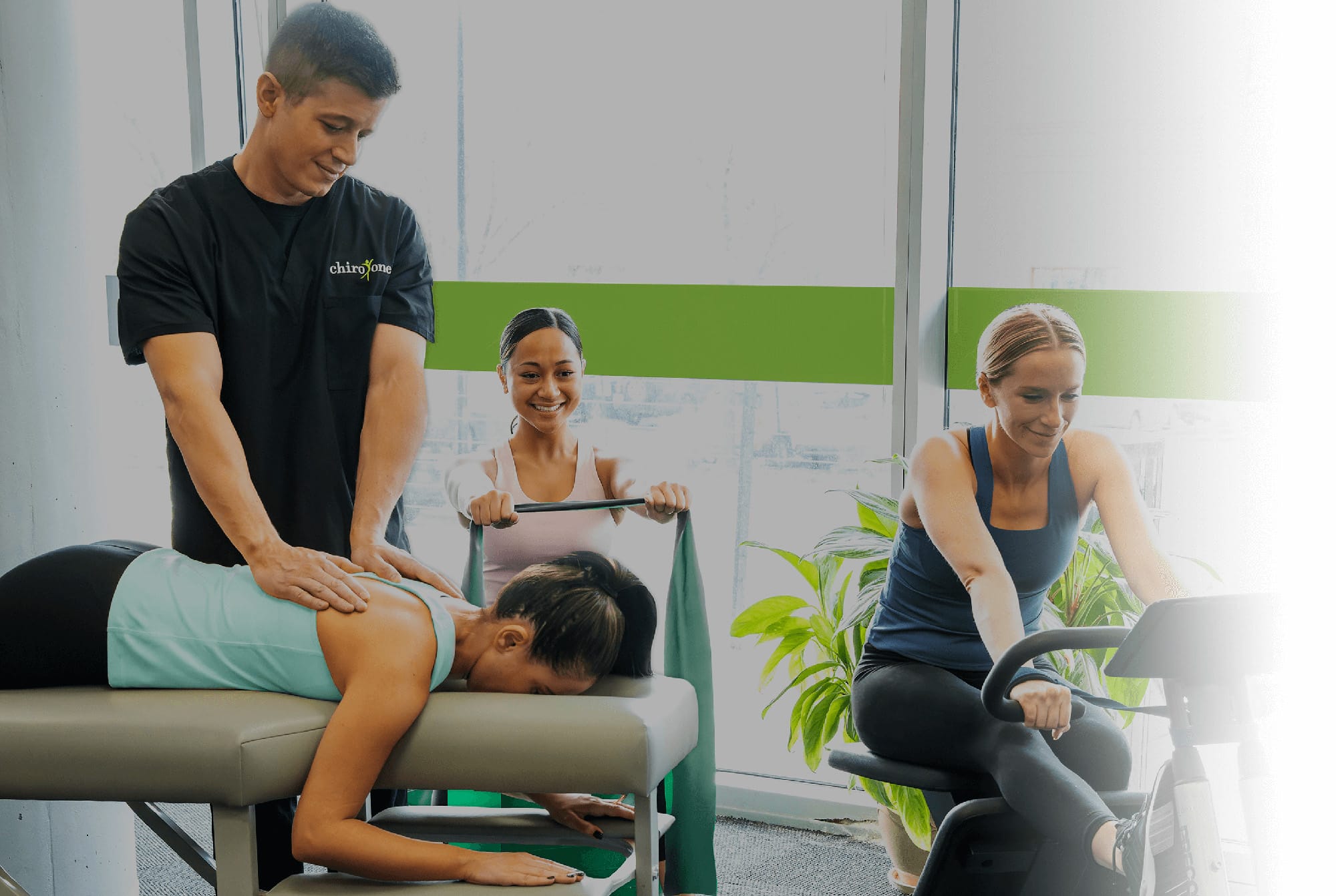 A woman receives a chiropractic adjustment at a Chiro One clinic while patients perform rehabilitative therapies nearby