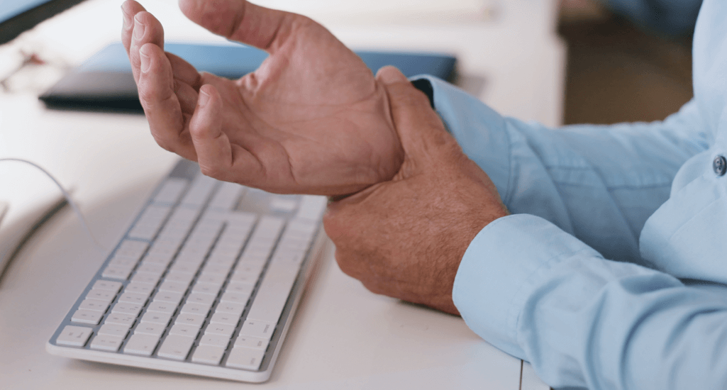 Man at desk clutching wrist in pain
