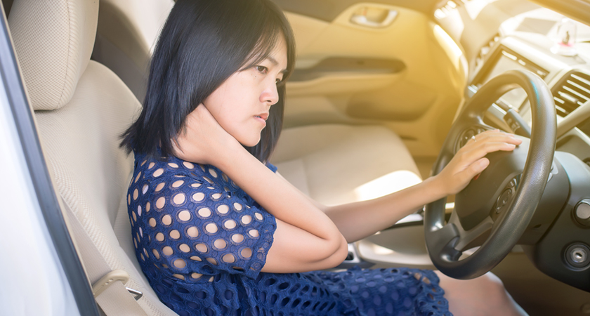 Woman behind wheel of a car with her hand gripping her neck