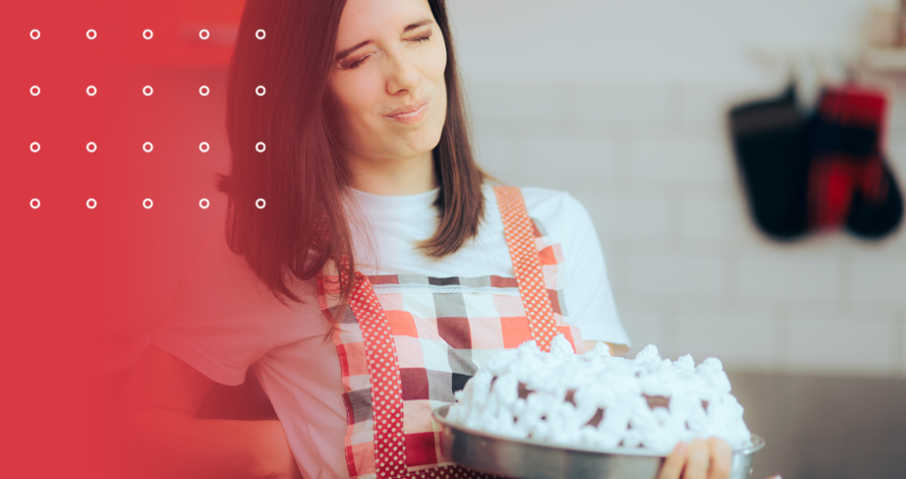 A stressed-looking woman in a kitchen apron holds a frosted cake, grimacing and clutching her lower back in pain, symbolizing the stress and physical strain of holiday preparations or back pain from baking.