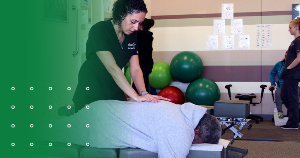 A female chiropractor is performing a chiropractic adjustment on a patient's upper back, who is lying face down on an adjustment table, illustrating back pain relief through spinal adjustments.