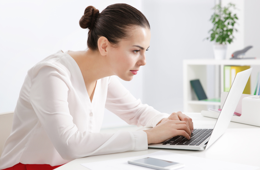 A woman sitting at a desk and leaning forward toward a laptop with poor posture.