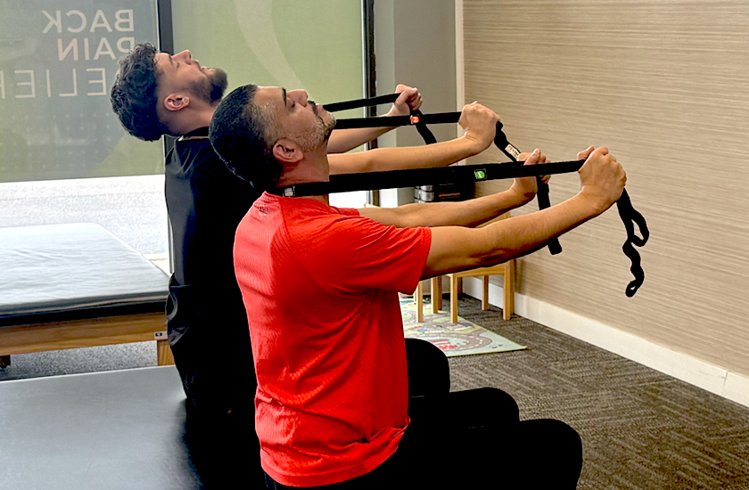 Two men at a Chiro One Wellness Center performing neck rehabilitation exercises.