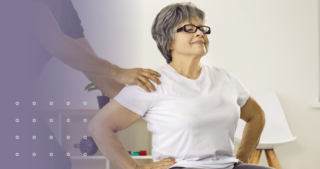 A chiropractor gently placing a hand on a senior woman’s shoulder during a postural assessment.