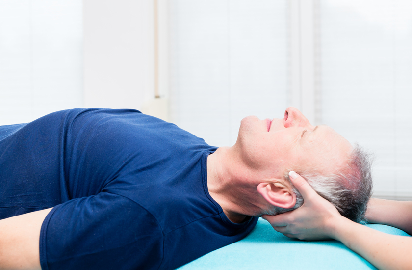 A senior man lying comfortably on a treatment table while a Chiro One chiropractor provides a gentle manual neck adjustment or supportive stretch.