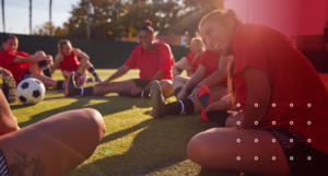 A women's soccer team in red uniforms stretching on the field to improve mobility and prevent soccer injuries, showcasing athletic wellness and conditioning.