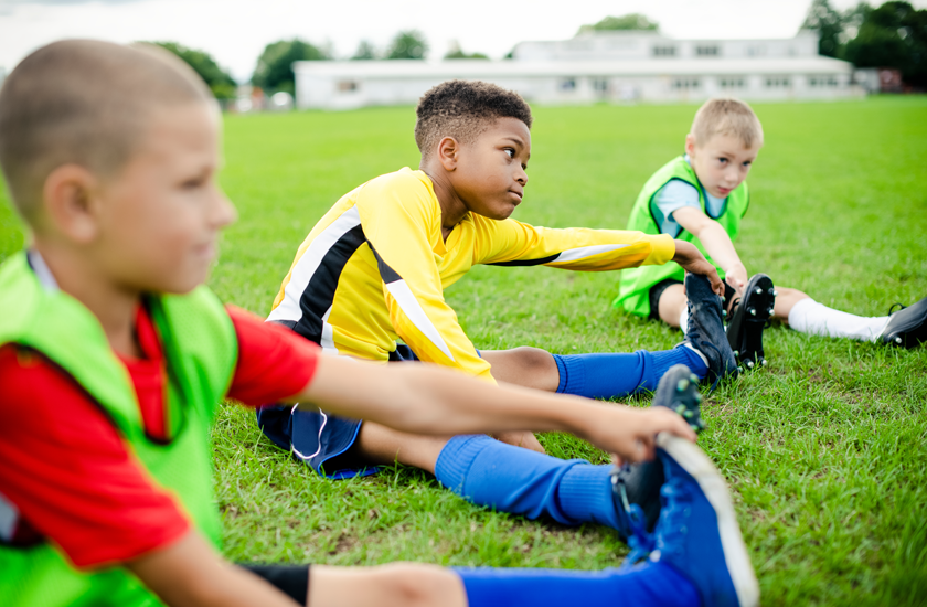 Young soccer players practicing hamstring stretches on a soccer field to maintain flexibility, reduce injury risks, and stay game-ready during the sports season.