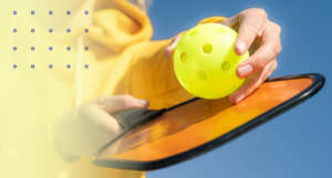A pickleball player holding a yellow pickleball and paddle, representing the growing popularity of the sport and the importance of injury prevention.