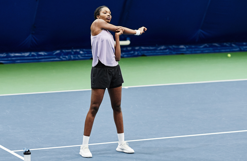 A woman stretching on a pickleball court to improve flexibility and reduce the risk of common sports injuries.
